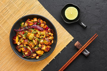 Kung Pao Paneer at black slate background. Kung Pao Paneer is a vegetarian version of chinese sichuan dish Gong Bao with paneer cheese, peanuts, chilli peppers, sauces and onion. Top view