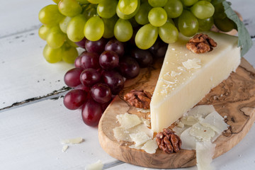 Pecorino romano, hard italian sheep milk cheese on wooden cutting board with grape, selective focus
