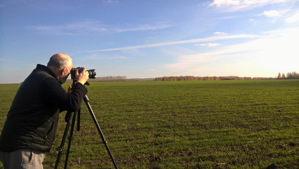 A male photographer in a black jacket takes pictures of a beautiful autumn landscape, clear sky and white clouds. Autumn, Indian summer. - Powered by Adobe