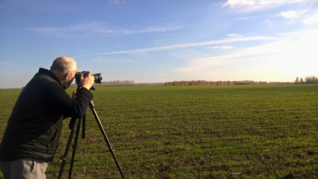 A male photographer in a black jacket takes pictures of a beautiful autumn landscape, clear sky and white clouds. Autumn, Indian summer.
