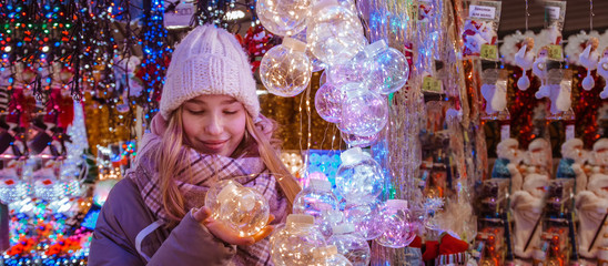 Girl walking in the Christmas market, a fair decorated with holiday lights in the evening. The mood of the winter holiday and comfort cozy . Winter Holidays.Long banner