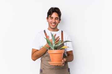 Young caucasian gardener man holding a plant isolated laughs out loudly keeping hand on chest.