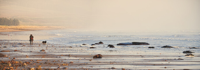 Woman with dog walking Brora beach in the Highlands of Scotland on the North Coast 500 route