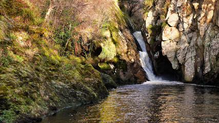 Glen Loth waterfall with early winter sunshine lighting the face of the cliffs towering above the waterfall pool