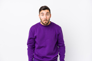 Young caucasian man against a white background isolated shrugs shoulders and open eyes confused.