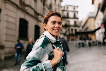 Happy smiling woman with blond hair wearing striped shirt walking on the sunny old street in Europe.