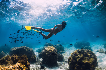 Freediver girl with fins glides over sandy bottom in blue ocean