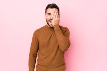 Young caucasian man against a pink background isolated having fun covering half of face with palm.