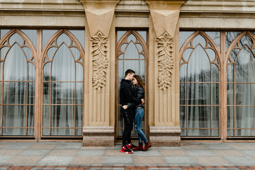 Attractive young couple walking near castle. Wife and husband kissing and holding hands on background of ancient building. Two smiling lovers. Family and love concept