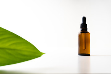 A small bottle with a dropper full of CBD oil or any other oil and a green leaf on white background