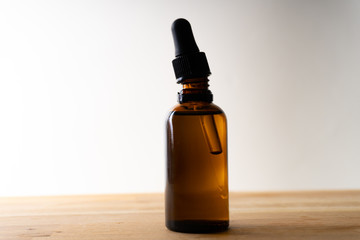 A small bottle with a dropper full of CBD oil or any other oil standing on a wooden board - white background