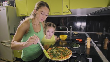 Mother teaching daughter smart girl learning to cook. Young mistress children to cook a Neapolitan egg fried omelette from salame affumicato sausage. Modern Built In Kitchen Appliances.