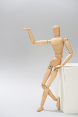 Wooden doll beside white stand point with hand on grey background
