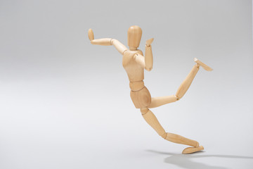 Wooden doll with raised hands and leg on grey background