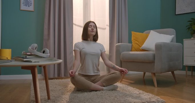 Caucasian beautiful young woman sitting on the floor of the living room and meditating with eyes closed at home. Inside.