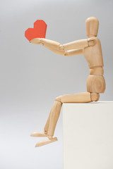 Wooden puppet with paper in heart shape on stand on grey background