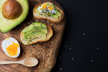 Avocado is a healthy food with organic eggs and sesame seeds placed on a wooden cutting board. On a black background
