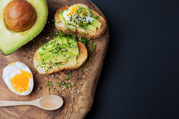 Avocado is a healthy food with organic eggs and sesame seeds placed on a wooden cutting board. On a black background