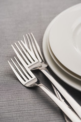 Shiny forks beside serving plates on grey tablecloth