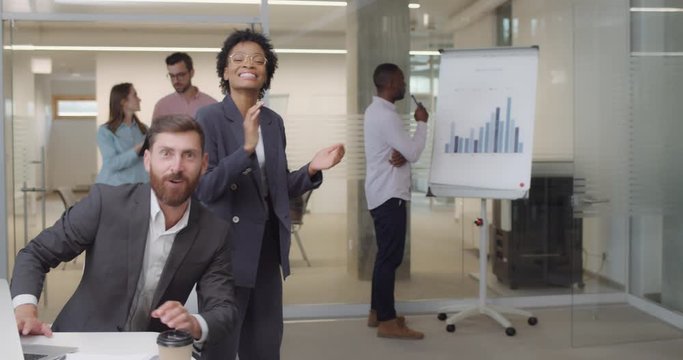 Happy multi ethnic workers standing in modern working space applouding and congratulating . Office staff looking happy meeting and greeting somebody , gesturing good. Camera view.