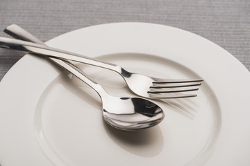 Close up view of shiny spoon and fork on plate on grey surface