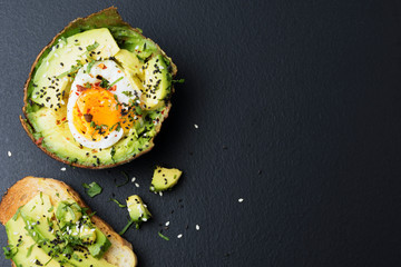 Avocado is a healthy food with organic eggs and sesame seeds laid on a black surface.