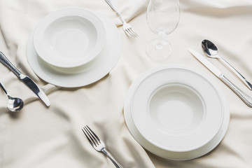High angle view of dinnerware with cutlery and wine glass on wavy tablecloth