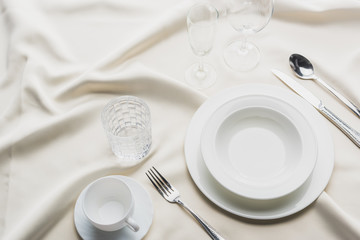 High angle view of dinnerware with glasses and coffee cup on white tablecloth