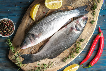 Fresh seabass and ingredients for cooking. Raw fish seabass with lemon, spices and herbs on blue wooden rustic table. Top view with copy space.