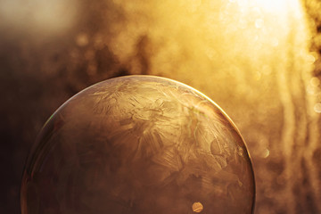 Frozen soap bubble in detail closeup on the background of the setting sun. Frosty patterns on the surface of the bubble. Image in warm yellow shades. Minimalism, background image.
