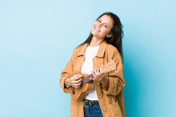 Young caucasian woman playing ukelele isolated on a blue background