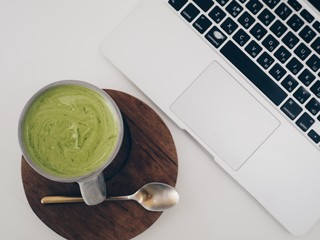 Top view laptop and ceramic cup of vegan beverage green tea matcha latte at white desk
