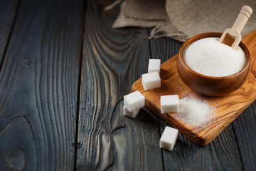 Wooden bowl with sugar on wooden plank on dark background
