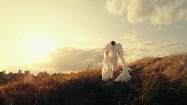 Angel goes to the top of the hill. Brunette girl in a white dress with angel wings goes to the top of the hill at sunset
