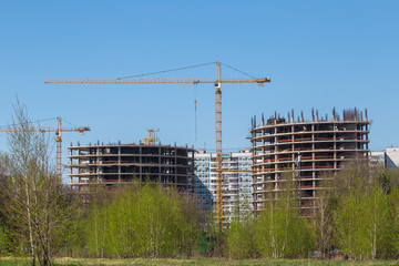 Obraz premium Industrial cranes on a background of high-rise buildings. Modern construction site. Modern industrial urban concept. Tower cranes constructing a new residential building.