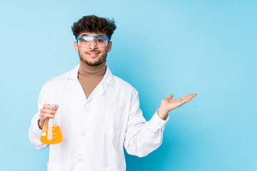 Young arab scientific man isolated showing a copy space on a palm and holding another hand on waist.