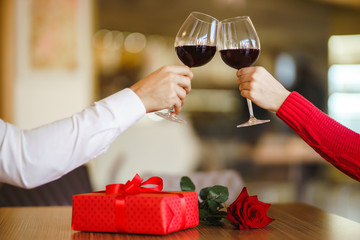 Hands holding glasses of wine on restaurant background. Couple clink glasses with red wine. Valentines day celebration concept. Relationship, surprise and love concept.