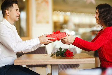 Man gives to his woman a gift box with red ribbon. A loving couple cuddles and celebrating...