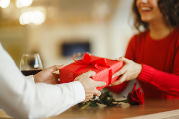 Man gives to his woman a gift box with red ribbon. A loving couple cuddles and celebrating...