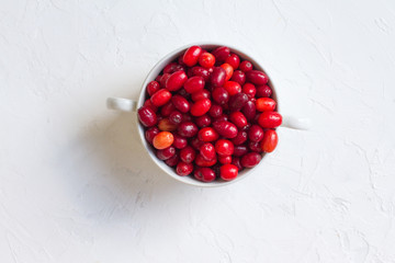 Dogwood is a sweet and sour red fruit. medicinal plant. ripe vitamin berries. Dogwood on a wooden white background in a white plate with space for text. The concept of a healthy lifestyle. gardening