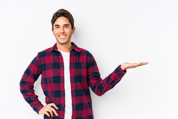 Young caucasian man posing in a pink background isolated showing a copy space on a palm and holding another hand on waist.