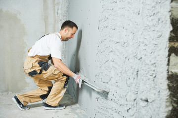 Plasterer using screeder smoothing putty plaster mortar on wall