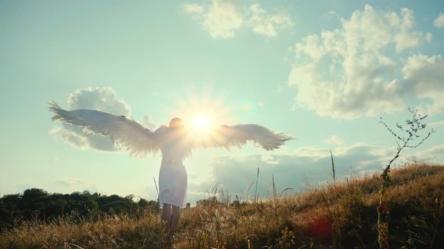 Rear view of beautiful girl angel on a hill raised its wings up and enjoys the sun and sunbeams