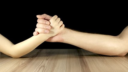 Father and son measure their strength, the boy defeats the man in arm wrestling. Closeup of men's and children's hands on wooden table and black background. Family hands clasped together.