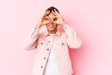 Young caucasian man posing in a pink background isolated showing okay sign over eyes