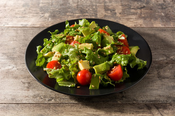 Salad with avocado, lettuce, tomato and flax seeds on wooden table