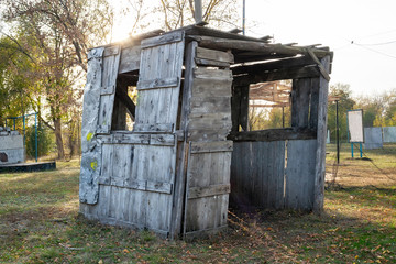 Fototapeta premium A rickety wooden shed of old boards and nails with spots of yellow paint is standing on the grass in the forest against the sun on a tactical paintball court