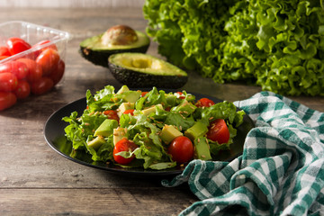 Salad with avocado, lettuce, tomato and flax seeds on wooden table