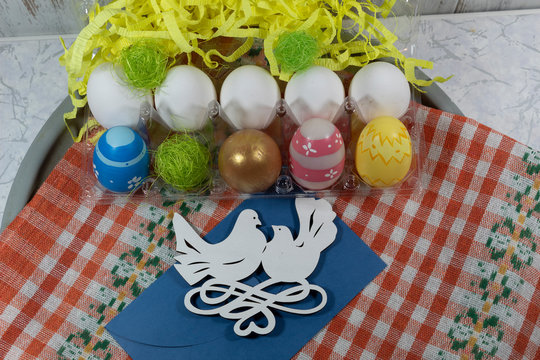 Painted and white eggs in a special shape for eggs. In the background are strips of yellow paper. In front is a blue envelope and an image of two white doves.