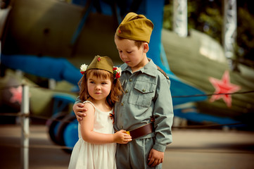 a boy of European appearance 6 years old in military uniform and a cute girl 4 years old in a white sundress, a reenactment of a meeting of a soldier with a bride, the theme of the great Patriotic war